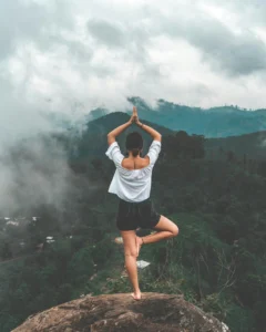 mujer parada en sobre una de sus piernas en una roca con un paisaje de fondo en pose meditativa meditaciones equilibrium