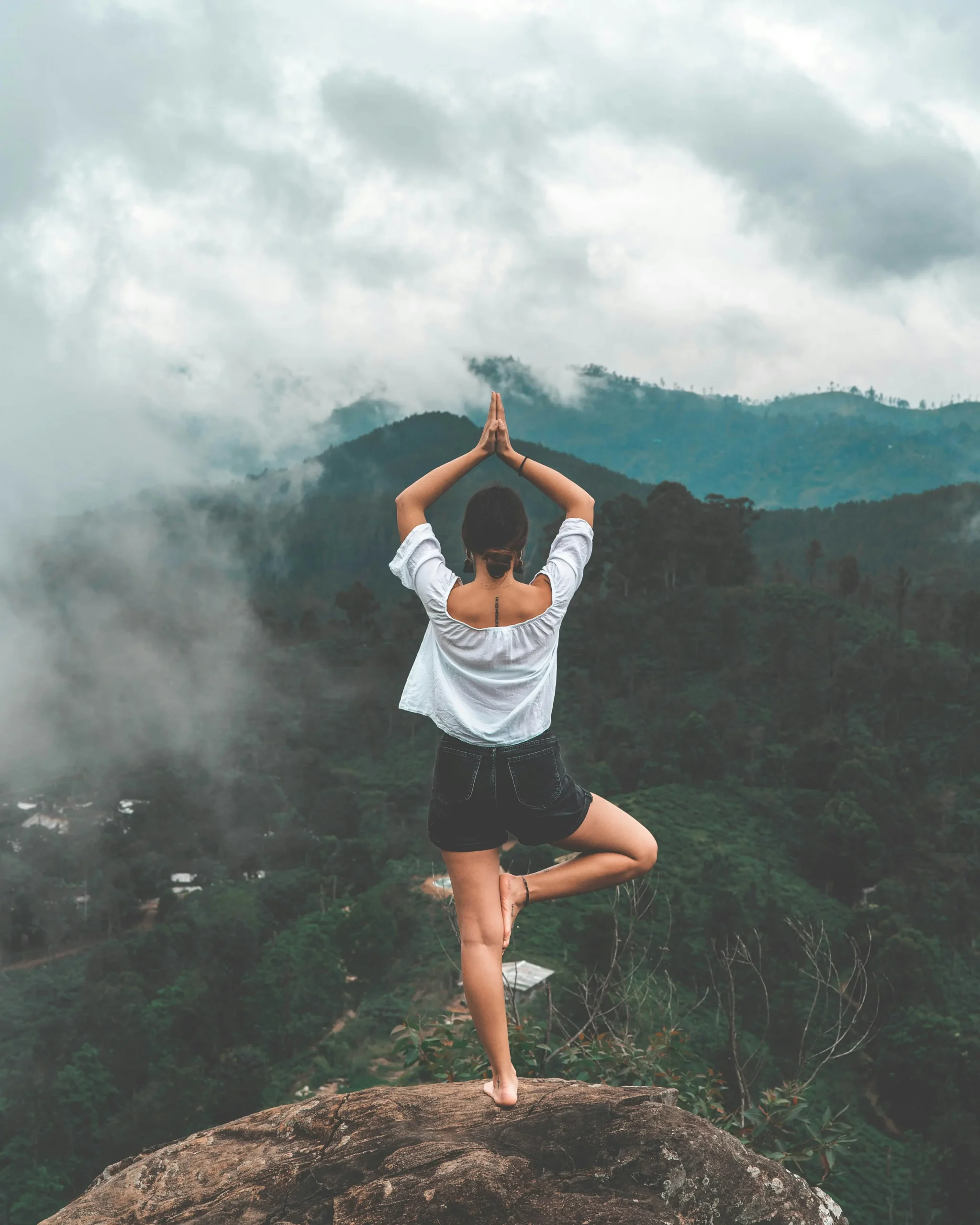 mujer parada en sobre una de sus piernas en una roca con un paisaje de fondo en pose meditativa meditaciones equilibrium